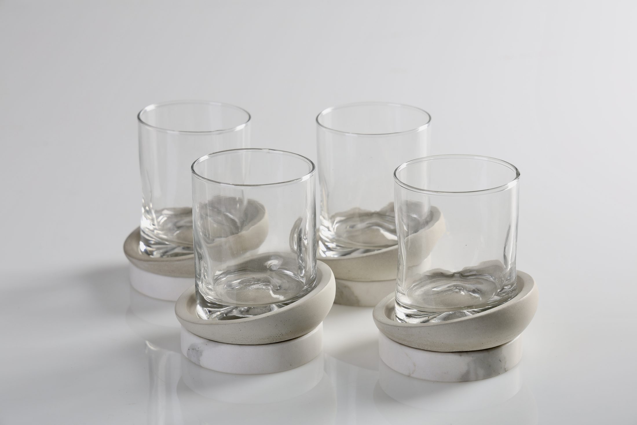 DOPPIO: cuatro vasos de vidrio, cada uno sobre un plato de concreto y mármol